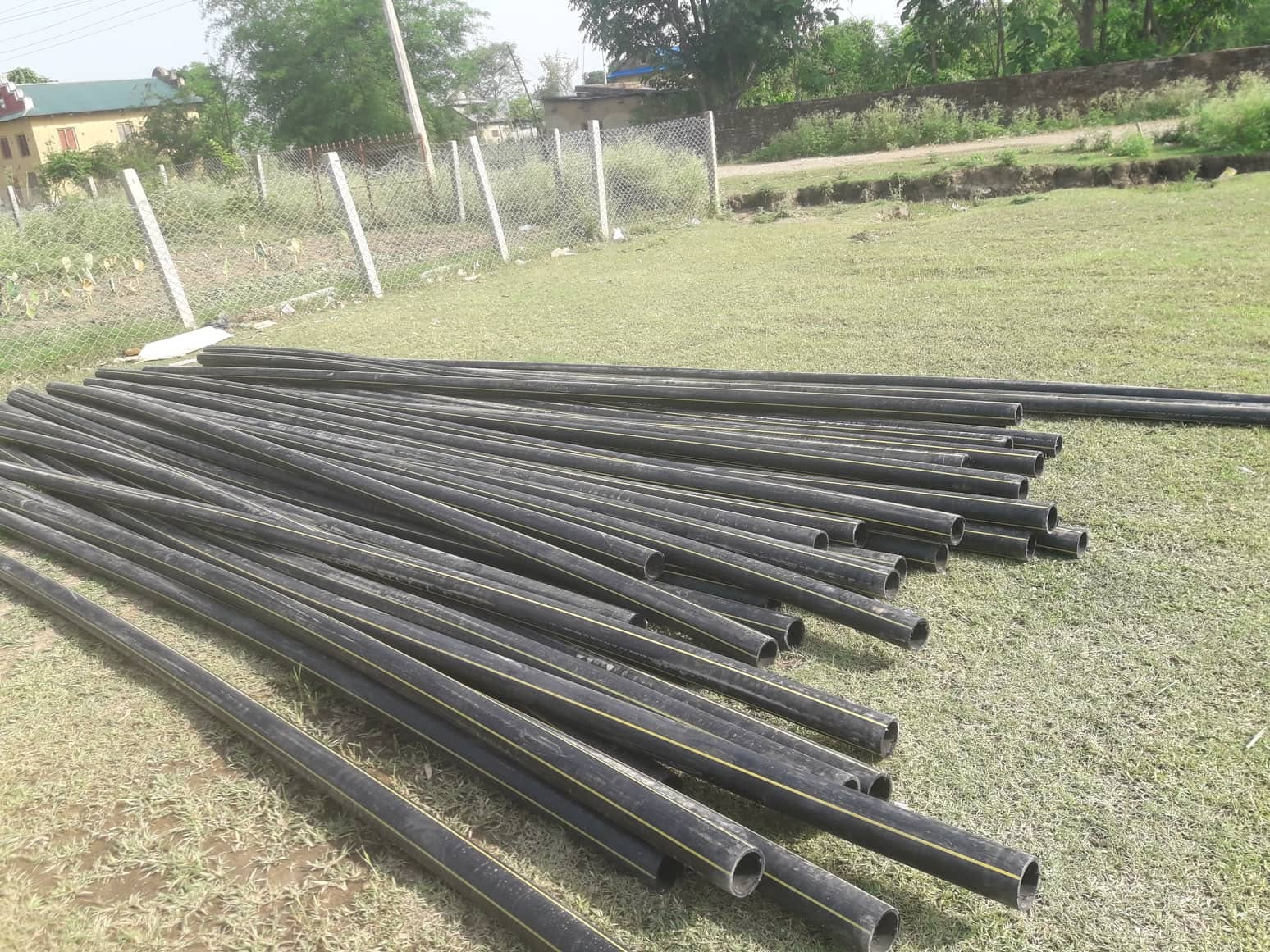 Black agricultural pipes stacked near a field